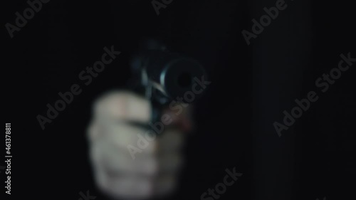 Unrecognizable assasin hitman with a silencer supressed silenced gun appearing from the shadows