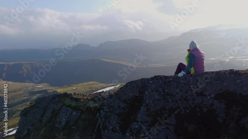 Aerial of hiker sitting on the mountain ridge admiring a landscape of summer mountain range still partially covered by snow photo