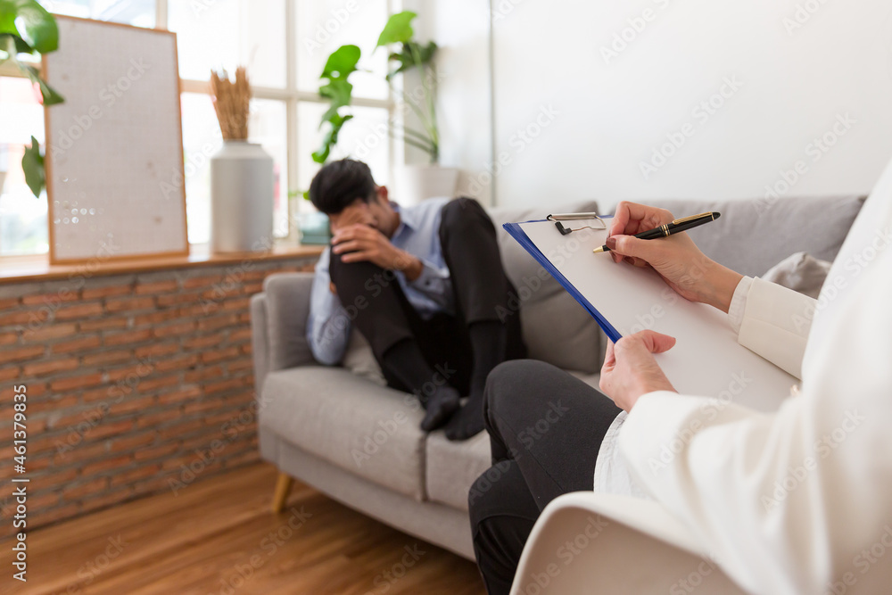 Young Asian man talking his problems with professional psychologist while conducting a consultation and making notes to seek advice and therapy Young Asian man talking his problems with professional psychologist while conducting a consultation and making notes to seek advice and therapy