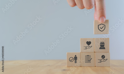 Safety at work concept. Hand holds wooden cube with safety icons; safety first, protections, health, regulations and insurance.  Used for banner, beautiful bright background and copy space. photo