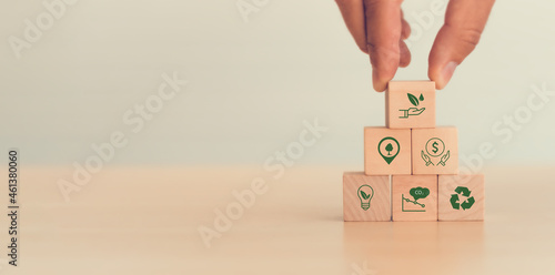 The concept of sustainability or environmental protection. Fingers hold wooden cube with sustainability, environment, green economy, renewable energy, CO2 emission, recycle icon with white background. photo