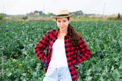 Portrait of young woman farmer in straw hat posing in farm field on sunny spring day