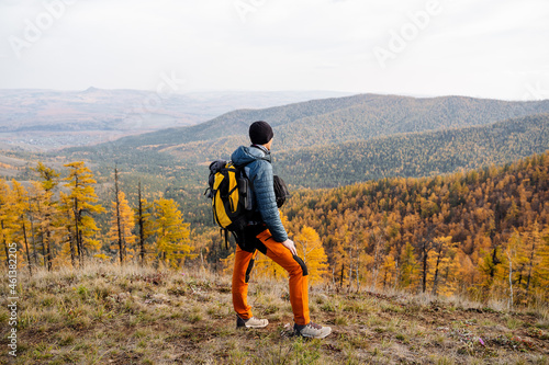A man stands on top of a mountain and looks at the landscape. Magnificent view of the autumn forest and mountains. Active rest, a trip to the mountains, autumn forest and golden faces.