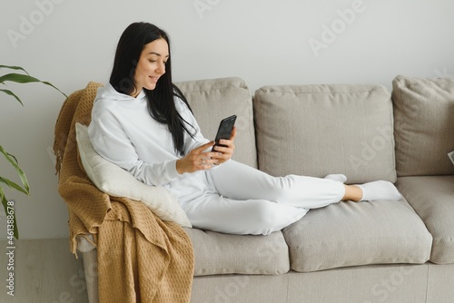 Portrait of a cheerful young woman using mobile phone while relaxing on a couch at home
