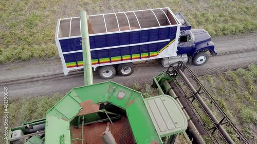 AERIAL - Combine harvester throws grain onto a truck, wide spinning shot photo