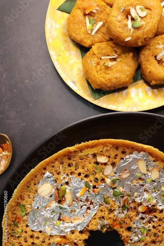 Rajasthani Ghevar. Ghewar is an Indian crunchy sweet dish made using refined flour, sugar, and ghee. Garnished with silver foil and dry fruits. Over dark background with copy space. photo