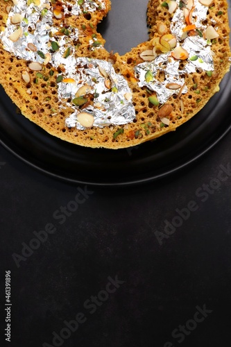 Rajasthani Ghevar. Ghewar is an Indian crunchy sweet dish made using refined flour, sugar, and ghee. Garnished with silver foil and dry fruits. Over dark background with copy space. photo