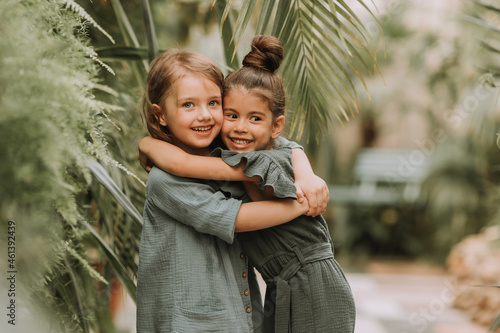 Portrait of two charming smiling girls belonging to different races surrounded by tropical leaves. Friendship, linen clothing, environmental friendliness. High quality photo