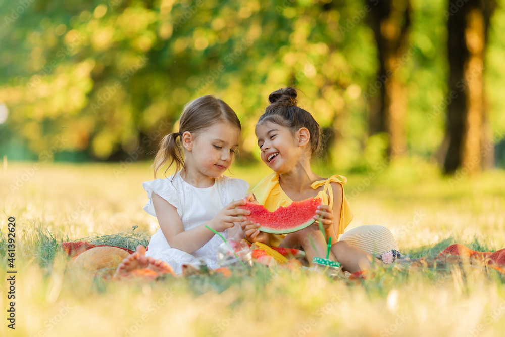 Girls are sitting on a blanket in the park and eat one slice of