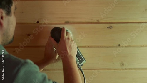 A man working with a grinding machine at the construction site. Male carpenter using a polishing machine for cleaning wooden log.