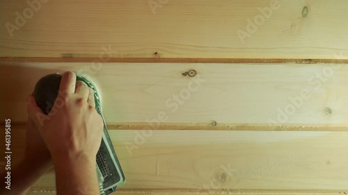 A man working with a grinding machine at the construction site. Male carpenter using a polishing machine for cleaning wooden log.