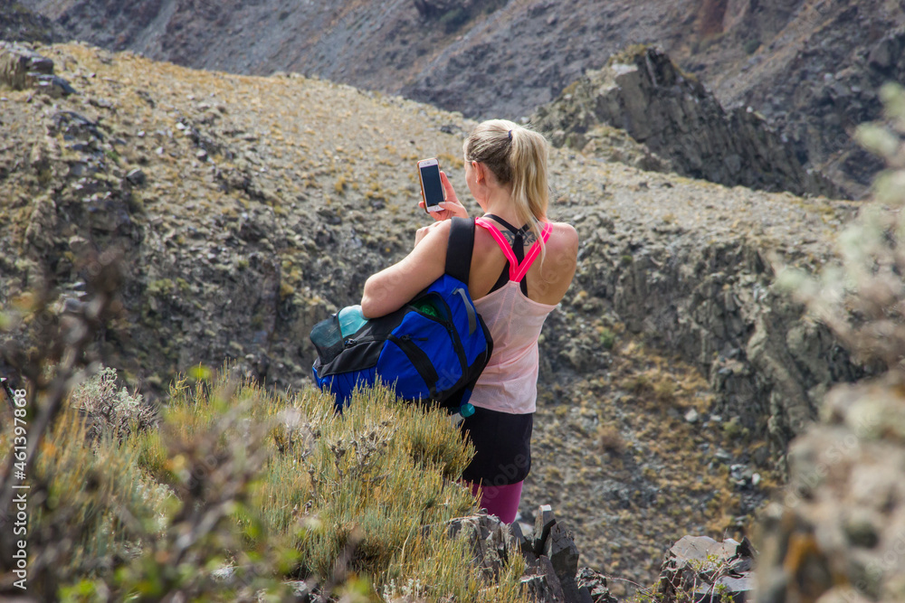 Young Caucasian female hiker taking photo with a smartphone in the mountains
