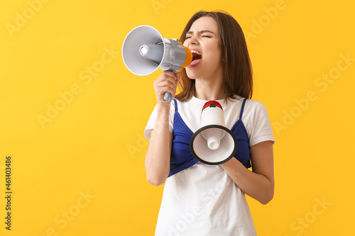 Protesting young woman with megaphones on color background