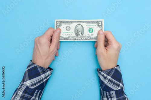 Man holds two dollars on a blue background. Financial literacy. Bankrupt. Money is tight. Importance of savings.