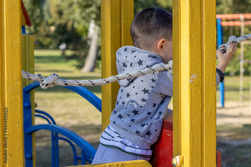 Fototapeta premium park,playground for kids,sunny summer day.kid is climbing and​ hanging​ from​ steel,iron, bars.iron rusted round rings,climbing rope ladder.slide, have fun, outdoor activities