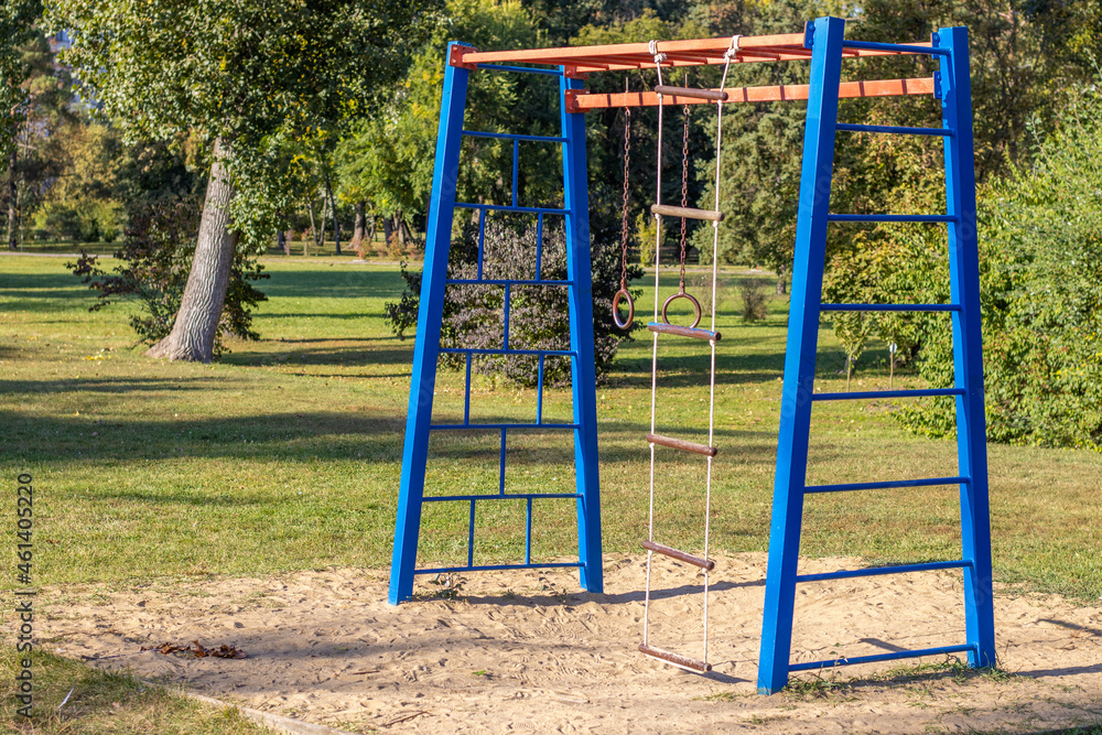 park,playground for kids,sunny summer day.kid is climbing and​ hanging​ from​ steel,iron, bars.iron rusted round rings,climbing rope ladder.slide, have fun, outdoor activities