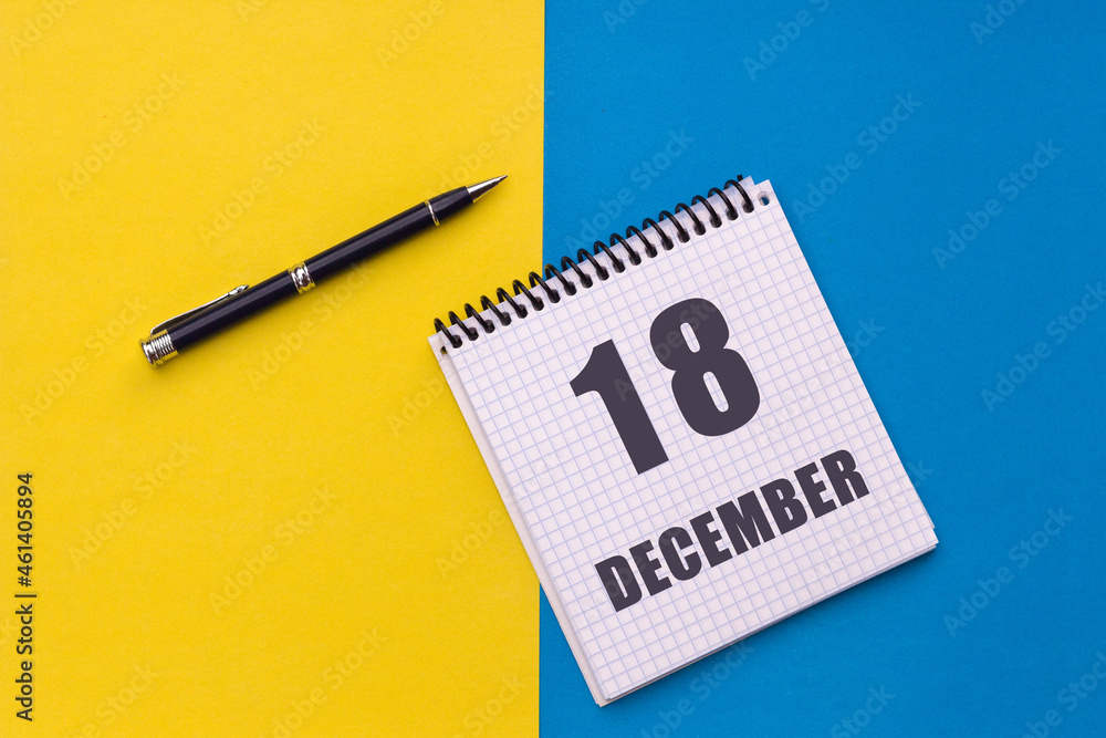 December 18th. Day 18 of month, calendar date. Notebook with a spiral and pen lies on a yellow-blue background December 18th. Day 18 of month, calendar date. Notebook with a spiral and pen lies on a yellow-blue background