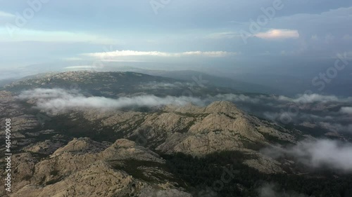 View from above, flying above the clouds, stunning aerial view of a granitic massif surrounded by moving clouds during a beautiful sunrise. Mount Limbara (Monte Limbara) Sardinia, Italy.	 photo