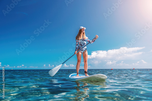 Healthy happy fit woman in bikini relaxing on a sup surfboard, floating on the clear turquoise sea water. Recreational Sports. Stand Up Paddle boarding. Summer fun, holidays travel. Active lifestyle photo