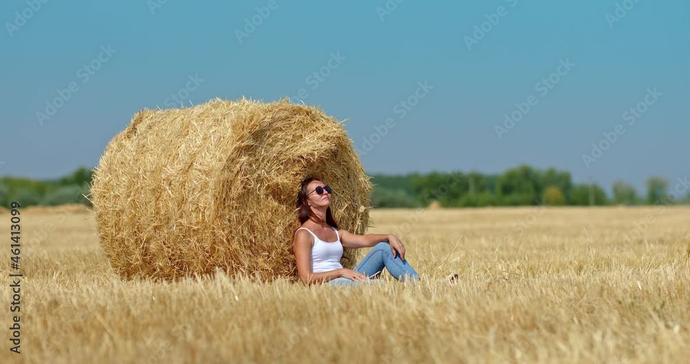 Beautiful girl is sitting by a haystack and enjoying nature. Girl is thoughtfully resting in a golden mown wheat field, a large haystack. Circular motion of the camera. 4k, ProRes Beautiful girl is sitting by a haystack and enjoying nature. Girl is thoughtfully resting in a golden mown wheat field, a large haystack. Circular motion of the camera. 4k, ProRes