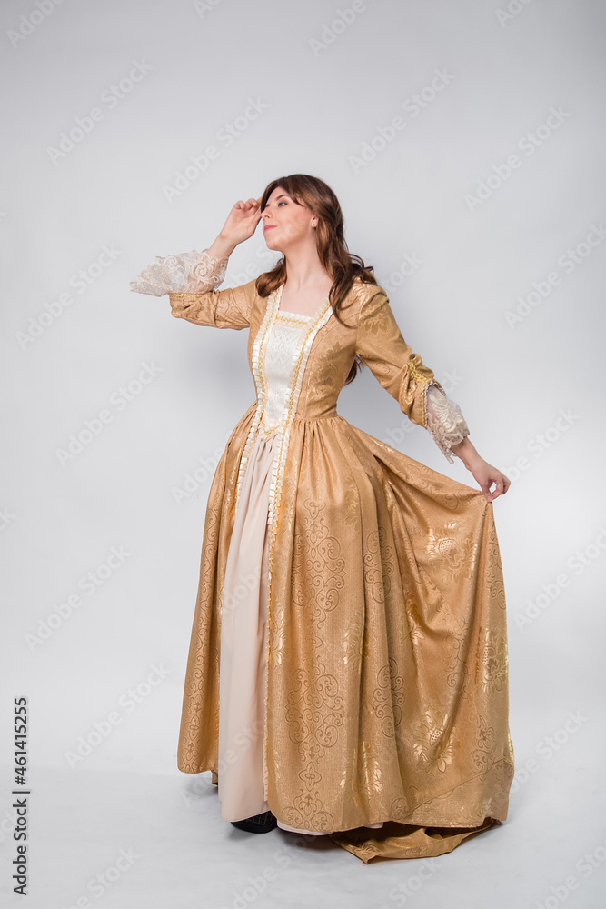 A full-length portrait of a girl in a golden rococo gown posing isolated on a white background. A full-length portrait of a girl in a golden rococo gown posing isolated on a white background.