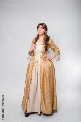 A full-length portrait of a girl in a golden rococo gown posing isolated on a white background.