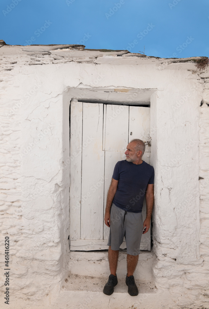 Adult man against white wooden door and white wall with blue sky