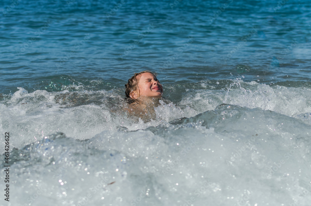 Little happy adorable girl child swims in the sea and plays on the waves during the holidays on the sea coast	
