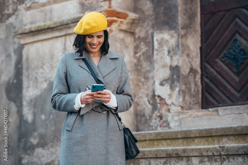 Woman using smartphone and wearing yellow beret and a gray coat