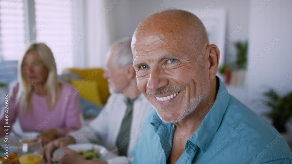 Senior man with friends having party indoors, eating at the table and looking at camera. Senior man with friends having party indoors, eating at the table and looking at camera.