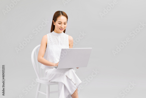 A young woman is sitting on the chair and working on the laptop.