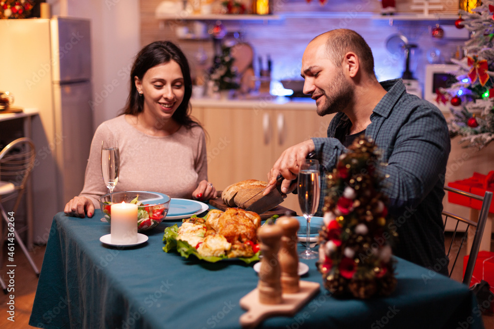 Married happy couple sitting at dining table in xmas decorated kitchen enjoying christmas winter dinner. Romantic cheerful happy celebrating christmas holiday. Santa-claus wintertime