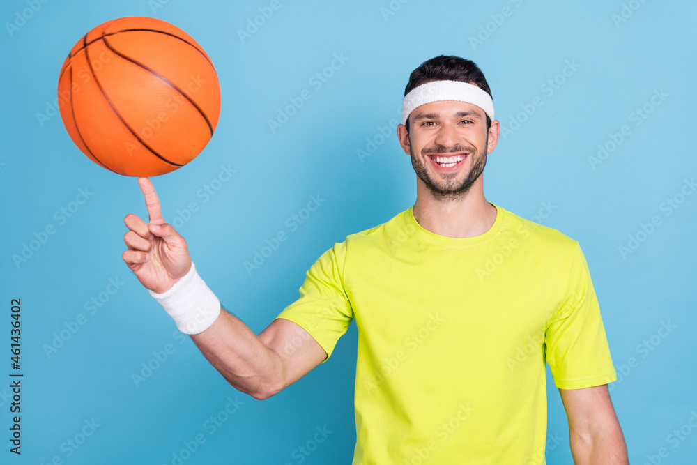 Portrait of attractive cheerful guy spinning ball on forefinger isolated over bright blue color background