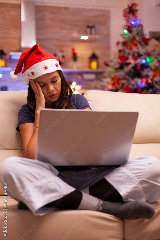 Tired exhausted woman falling asleep on couch in xmas decorated kitchen while reading business email on computer. Caucasian female celebrating christmas holiday enjoying winter season Tired exhausted woman falling asleep on couch in xmas decorated kitchen while reading business email on computer. Caucasian female celebrating christmas holiday enjoying winter season