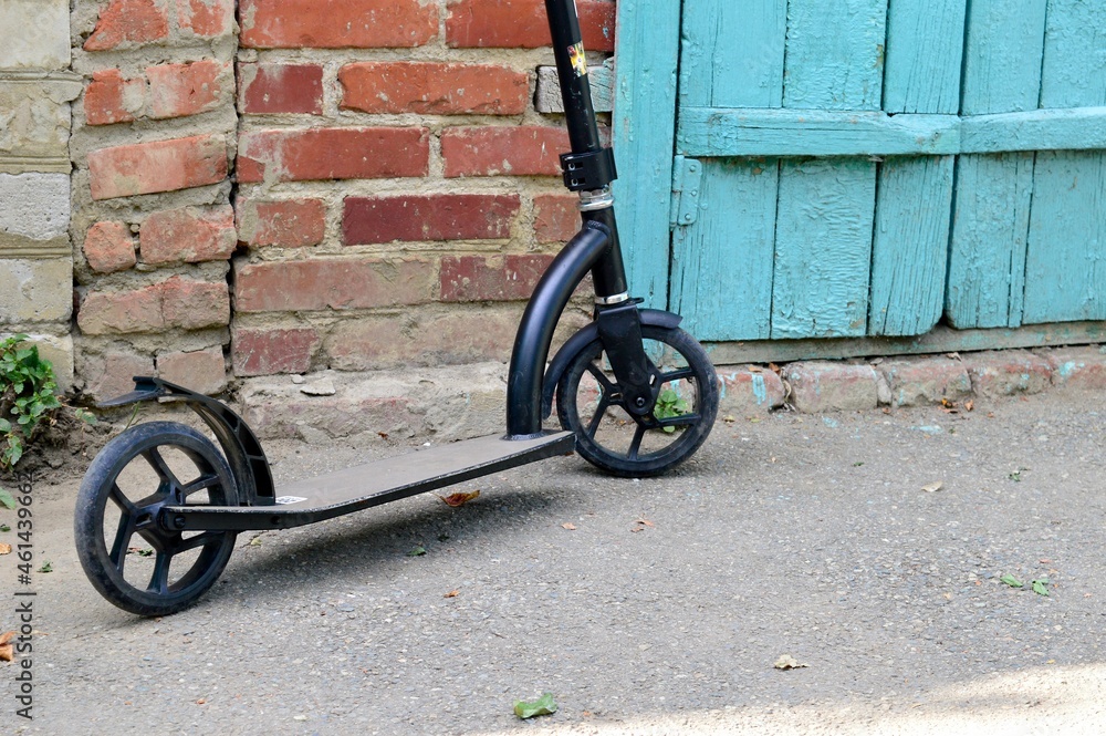 A black scooter stands against a brick wall in the yard.