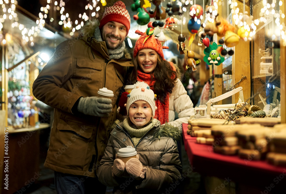 family, winter holidays and celebration concept - happy mother, father and little daughter with takeaway drinks at christmas market on town hall square in tallinn, estonia over lights