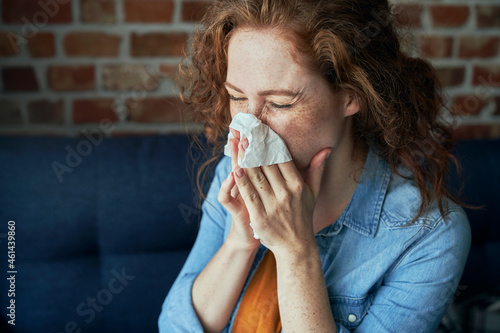 Young caucasian  red head woman blowing nose into tissue at home photo