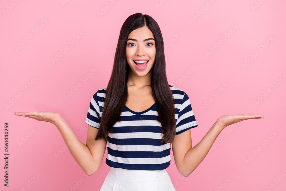 Photo of astonished long hairdo young lady hold empty space wear striped t-shirt isolated on pastel pink color background Photo of astonished long hairdo young lady hold empty space wear striped t-shirt isolated on pastel pink color background