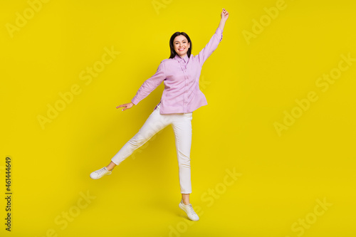 Full size photo of funny brown hairdo young lady jump arm up wear pink shirt pants isolated on yellow color background