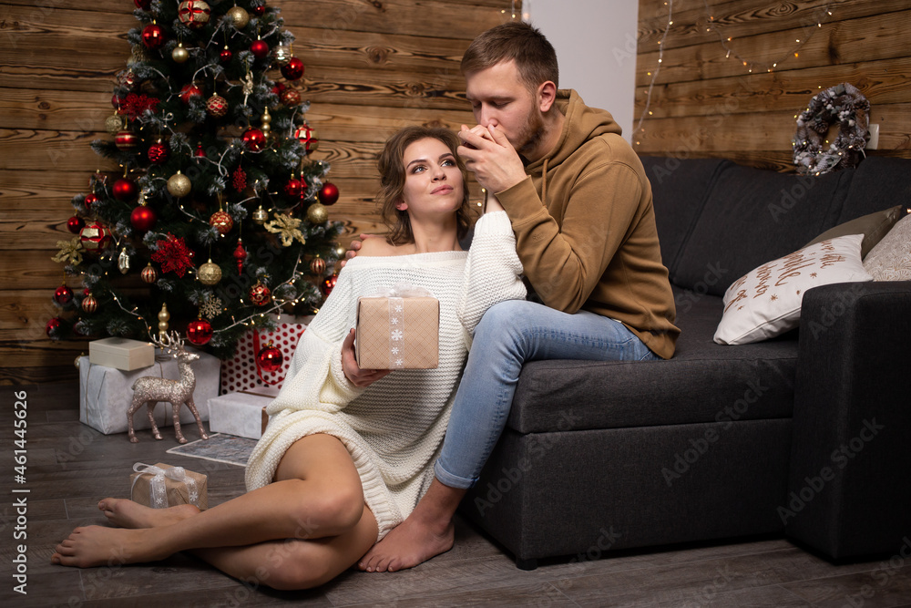 Obraz premium young couple with gift box enjoying their time together at home. Christmas tree on background.