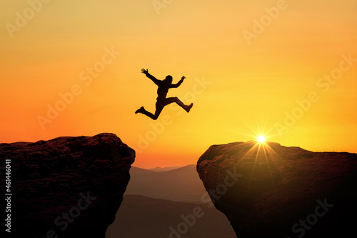 Man jumps from cliff to cliff over a precipice at sunset, a creative idea. Success and Risk Concept