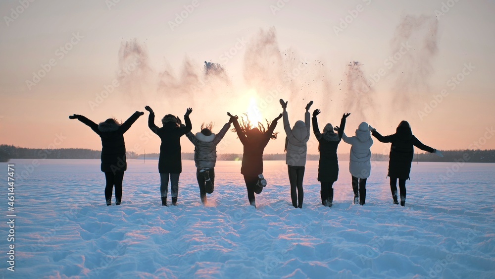 Fototapeta premium A group of girls friends are throwing snow up at sunset.
