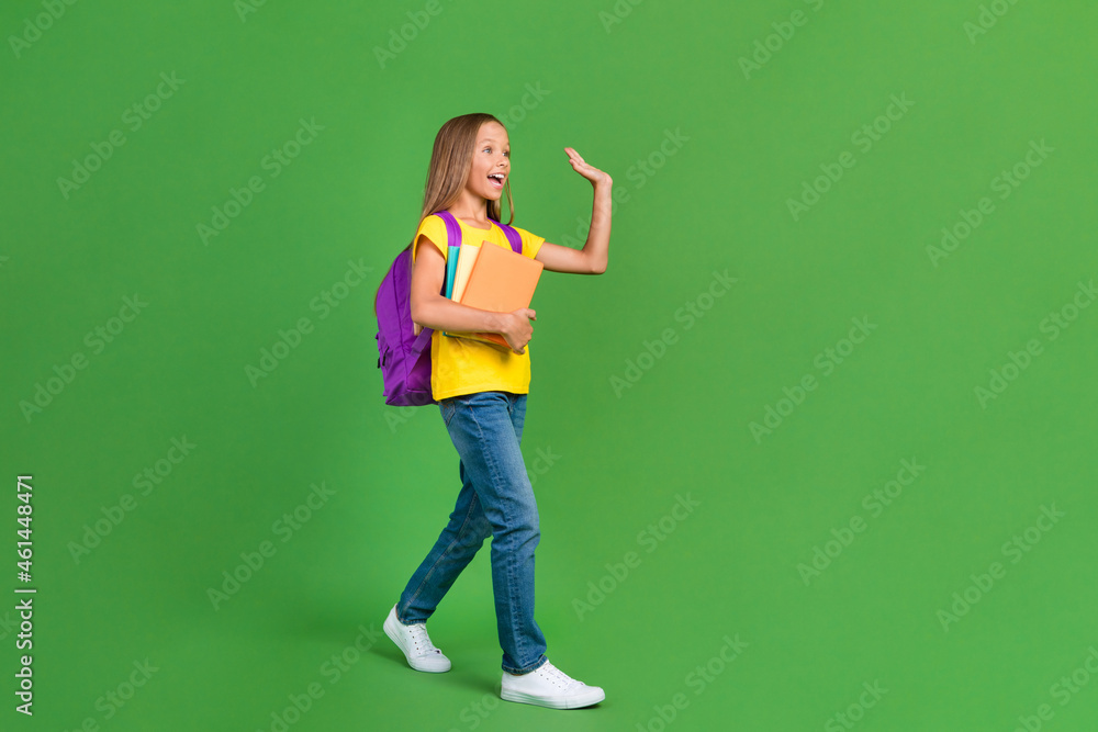 Full length body size view of pretty cheerful girl going to college waving hi hello isolated over vivid green color background Full length body size view of pretty cheerful girl going to college waving hi hello isolated over vivid green color background