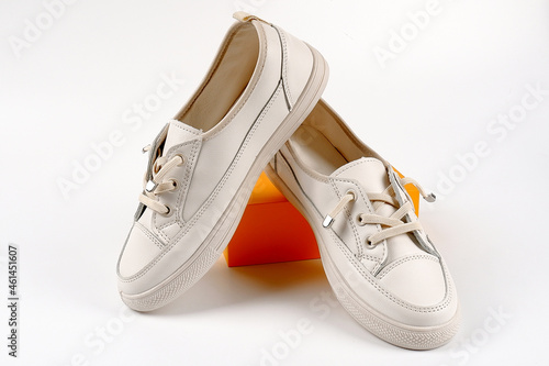 Casual comfortable white shoes.Stylish women's leather sports shoes with laces on a yellow box. Seasonal sales, promotions, discounts on shoes. Proper care for white skin.