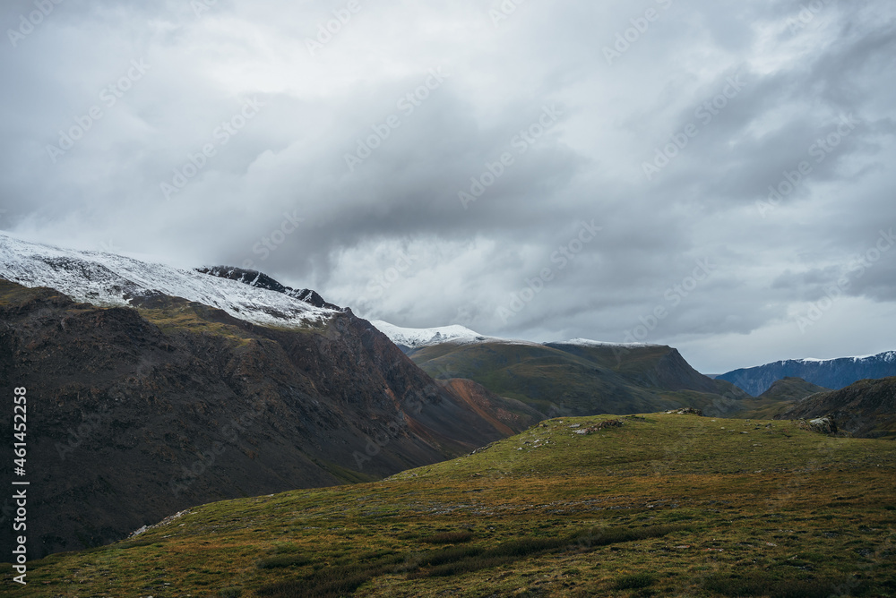 Atmospheric alpine landscape with deep gorge and snow-capped multicolor mountains in overcast weather. Beautiful scenery with snowbound mountain range under cloudy sky. Motley high mountains with snow Atmospheric alpine landscape with deep gorge and snow-capped multicolor mountains in overcast weather. Beautiful scenery with snowbound mountain range under cloudy sky. Motley high mountains with snow