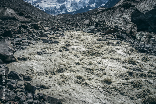 Scenic highlands landscape of powerful mountain river beginning from glacier among large moraines. Beautiful scenery with glacier at source of turbulent river. Mountain river source among big stones.