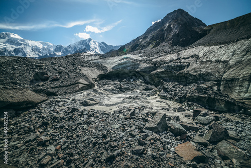 Scenic highlands landscape with big cracked glacier with scratches among moraines on background of high snowy mountain peak and rock top. Awesome scenery with large glacier and great snowy mountain.