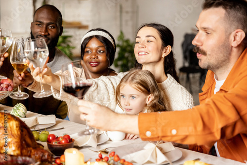 Close-up happy multiethnic big family celebrate Thanksgiving day, sitting at table with roasted turkey and holiday traditional food, dishes.