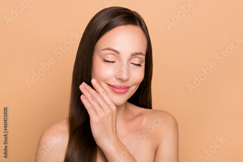 Photo of dreamy pretty mature woman naked shoulders arm cheekbone closed eyes smiling isolated beige color background