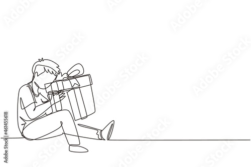 Single one line drawing cheerful boy sitting and hugging big gift box with ribbon bow wrapped in front of his in arms. Little kid accept birthday gift. Continuous line draw design vector illustration